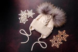 Beautiful white knitted winter cap with pompons on a dark concrete background photo