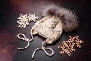 Beautiful white knitted winter cap with pompons on a dark concrete background photo