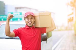 joven feliz llevando un paquete en el servicio de mensajería postal al entregar el paquete. foto