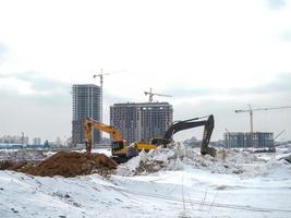 Construction of high-rise buildings in winter. The work of excavators. Land works. Digging pits. photo