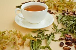 herbal tea in a white cup for beauty and health, dried herbs, linden flowers and strawberries lie around. photo