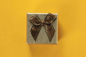 Top view of Mini golden gift box with ribbon on yellow background, close up view of gift box for Merry New Year and Merry Christmas 2023 concept.