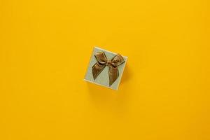 Mini golden gift box with ribbon on yellow background, giving special gift box for Merry New Year and Merry Christmas 2023 concept, yellow gift box on top view.