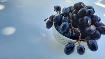 uvas moradas en un tazón con tallo aislado sobre fondo blanco y sombra 02 foto