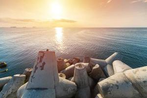 Beautiful sunset seascape. Travel dreams and motivation. Breakwaters tetrapods on shore of pier. Cargo ships on the horizon. photo