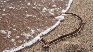 as ondas do mar rolam na praia com a imagem de um coração. video