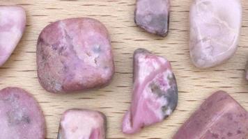 Rhodochrosite rare jewel stones texture on light varnished wood background. Moving right seamless loop backdrop. video