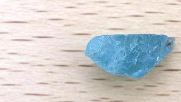 Apatite jewel stone texture on light varnished wood background. Macro closeup. Moving right seamless loop backdrop. video