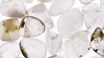 Rutilated quartz heap jewel stones texture on white light background. Moving right seamless loop backdrop. video