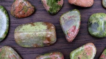 Unakite rare jewel stones texture on brown varnished wood background. Moving right seamless loop backdrop. video