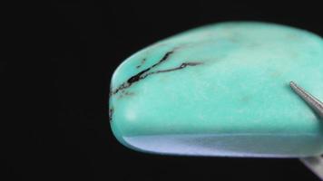 Turquoise jewel stone texture in tweezers on black background. Macro closeup. Moving right seamless loop backdrop. video