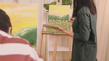 une enseignante asiatique experte enseigne et montre aux élèves la peinture acrylique couleur sur toile dans une salle de classe d'art, apprenant de manière créative avec compétence dans l'enseignement en studio de l'école primaire. video