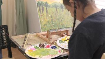 la petite fille se concentre sur la peinture acrylique sur chevalet en toile avec un enseignant et des enfants dans une classe d'art, l'enseignement en studio à l'école primaire avec des compétences créatives, une mise au point sélective sur une image. video