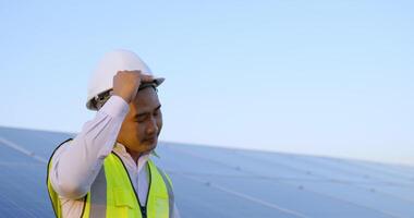 jovem engenheiro asiático tira o capacete e sorri durante uma pausa na fazenda solar, painéis solares em segundo plano video