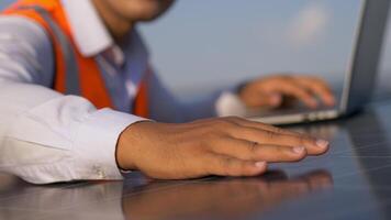 selectief focus, jong Aziatisch technicus Mens controle operatie van zon en netheid van fotovoltaïsche zonne- paneel en typen Aan laptop computer terwijl werken in zonne- boerderij video