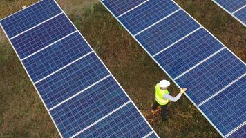 Rotate Shot, Aerial drone view, Flight over solar panel farm, young engineer wearing helmet checking on operation of sun and cleanliness of photovoltaic solar panels at sunset