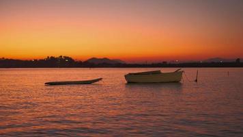 filme 4k em tempo real, pôr do sol na baía, silhueta de um barco no fundo da baía, peixes pulando fora d'água, férias no mediterrâneo video