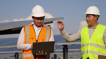 Asian Inspector Engineer man use laptop computer and young technician man come in and they are discussing and looking in laptop during working at solar farm, solar panel in background video