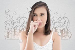 Asian woman in white dress catch her nose because of a bad smell against gray background photo