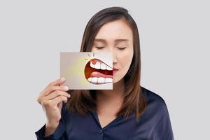 mujer asiática sosteniendo un papel con la caricatura periodontal y gingivitis de su boca contra el fondo gris, diente cariado, el concepto con encías y dientes de salud foto