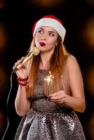 Joven mujer atractiva rubia en rojo sombrero de año nuevo con micrófono y bengala cantando en el escenario foto