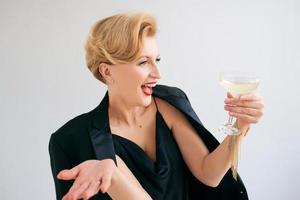 Laughing Caucasian mature stylish elegant woman in tuxedo with glass of sparkling wine. Party, celebration, anti age concept photo