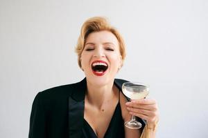 Riendo caucásica mujer madura elegante con estilo en esmoquin con una copa de vino espumoso. fiesta, celebración, concepto anti edad. foto