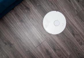 a white vacuum cleaner robot on a laminated wooden floor. photo