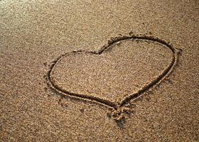 Heart on a sand of beach with wave on background photo