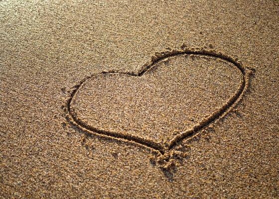 Heart on a sand of beach with wave on background
