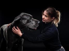una joven mujer bonita posa con su mascota, un gran danés, resaltada en un fondo negro. foto