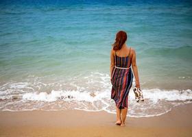 feliz joven boho mujer caminando y divirtiéndose en las olas del mar en un día cálido y soleado en una isla tropical. foto