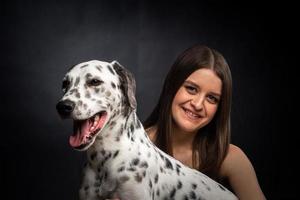 una joven mujer bonita está jugando con su mascota dálmata, aislada en un fondo negro. foto