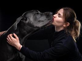 young pretty woman poses with her pet, a Great Dane, highlighted on a black background. photo