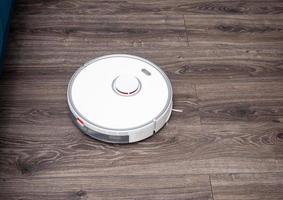 a white vacuum cleaner robot on a laminated wooden floor. photo