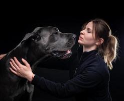 young pretty woman poses with her pet, a Great Dane, highlighted on a black background. photo