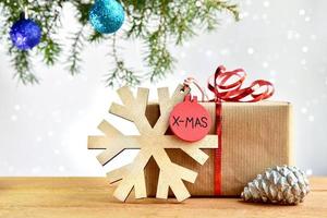 composición navideña con un regalo, un colgante de madera con un copo de nieve y un cono de pino en el fondo de un árbol de navidad y luces bokeh.