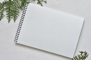 watercolor white sketchbook on a black spring lying on a linen tablecloth with sprigs of green thuja photo