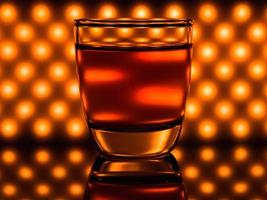 Glass of whiskey and orange lights on the background photo