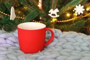 taza roja en blanco con árbol de navidad en el fondo, taza de té o café con decoración de navidad y año nuevo, maqueta horizontal con taza de cerámica para bebidas calientes, plantilla de impresión de regalo vacía. foto