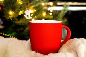 taza roja en blanco con árbol de navidad en el fondo, taza de té o café con decoración de navidad y año nuevo, maqueta horizontal con taza de cerámica para bebidas calientes, plantilla de impresión de regalo vacía. foto