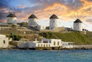 molinos de viento de mykonos frente a una espectacular puesta de sol iluminando las nubes con color en el fondo. foto