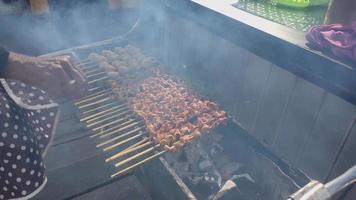 iemand grillen gehaktballen en kip darmen spies met bamboe, voor uitverkoop Bij een culinaire festival video