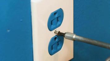 Installing a black socket housing on an old blue wall socket on a concrete wall, close-up. Bottom view. Unrecognizable contractor uses a screwdriver to detach plastic sockets from the blue wall. video