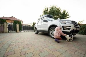 Girl playing with his cat in the yard of house, near family car. photo