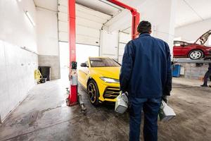 Mechanic stand with oil bottles against yellow sport car suv. photo
