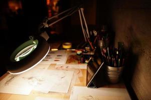 Desk with turn on lamp and painting items. photo