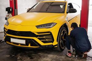 el mecánico comprueba la presión de los neumáticos en un coche deportivo amarillo suv. foto