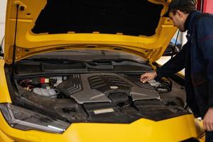 Mechanic open hood of yellow sport car suv. photo