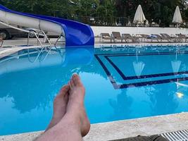 Man's feet on the background of a swimming pool. man relaxing by the pool, men's feet on the pool background photo